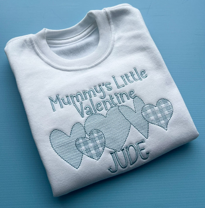 Folded white sweatshirt with embroidered text and hearts on a blue background